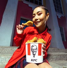 a woman sitting on the steps eating some food from a bucket with kfc logo