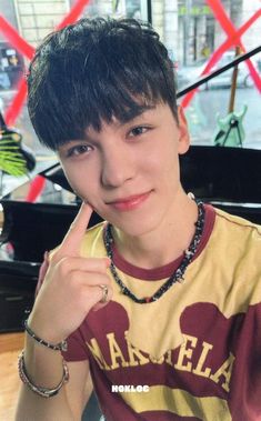 a young man posing for the camera in front of a black piano and wearing a necklace