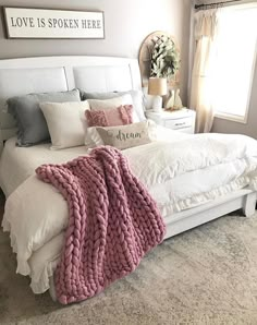 a white bed topped with a pink blanket next to pillows and blankets on top of it