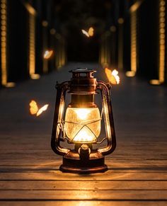 a lantern lit up on a wooden walkway with butterflies flying around it at night time