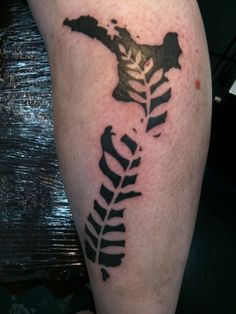 a tattoo on the leg of a person with a cross and fern leaf in it