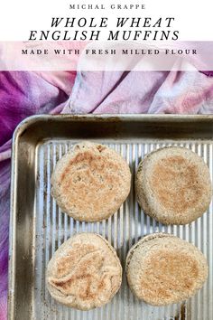 three whole wheat english muffins on a baking sheet with text overlay that says whole wheat english muffins made with fresh mixed flour