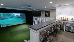 a golf simulator is set up in the middle of a kitchen with bar stools