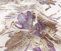 a white and purple fabric with gold leaf designs on it's side, in close up