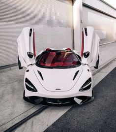 a white sports car with its doors open sitting on the street next to a garage