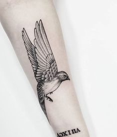 a small bird tattoo on the arm with words written below it and an arrow in the middle