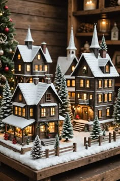 a christmas village is shown with trees and lights on the snow - covered ground in front of a wooden wall