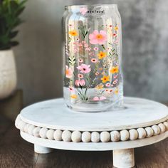 a glass jar with flowers painted on it sitting on a table next to a potted plant