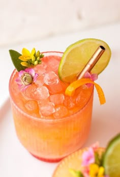 a close up of a drink in a glass on a plate with limes and flowers