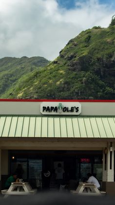 two people sitting at picnic tables in front of a papapole's restaurant with mountains in the background