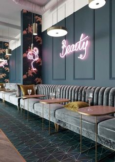 the interior of a restaurant with grey couches and neon signs on the wall behind them