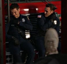 two police officers sitting on the back of a firetruck talking to each other