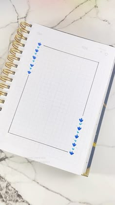 an open spiral notebook on a marble surface with blue hearts drawn on it and the cover is lined in gold foil