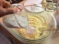 a person pouring batter into a glass bowl on top of a counter with utensils