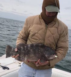 a man holding a large fish in his hands on a boat with the hood up