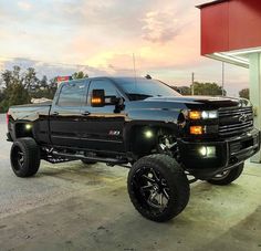 a black pickup truck parked in front of a gas station at dusk with the lights on