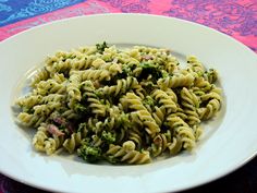 a white plate topped with pasta and broccoli on top of a colorful table cloth