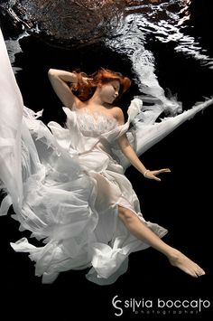 a woman floating in the water wearing a white dress