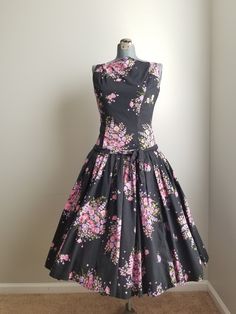 "Gorgeous 1950's dress with extremely full, pleated skirt and dropped waist. The bodice has a high neckline.The fabric is a black based floral cotton with pink and purple flowers. This dress is handmade and it is fairly obvious. There have been mends, and there may need to be a few more. There is a popped seam (quick, easy fix). Note: dress displayed with crinoline. Condition: Good vintage condition. Needs a repair of a seam or two (see photo). The handmade nature, means things aren't perfect, b Vintage A-line Dress With Pleated Bodice, Fitted Black Dresses With Accordion Pleats, Vintage Dresses With Pleated Bodice And Tea Length, Vintage Tea Length Dress With Pleated Bodice, Vintage Dresses With Pleated Bodice For Vintage Events, Vintage A-line Pleated Dress, Vintage Dress With Box Pleat For Vintage Fashion, Vintage Dresses With Box Pleat, Vintage A-line Dress With Pleated Waist