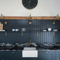 a kitchen with black cabinets and a clock on the wall over the sink, along with marble counter tops