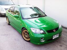 a green car is parked in front of a white wall and two other cars are behind it