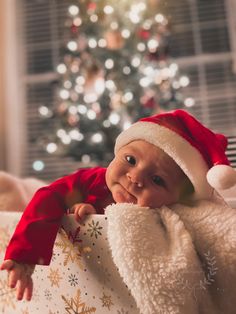 a baby wearing a santa hat and holding a christmas present in front of a christmas tree