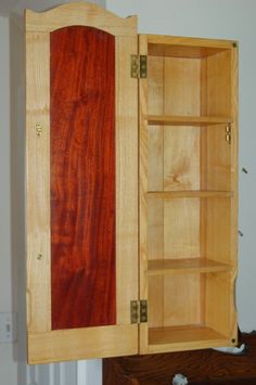 a wooden cabinet with two doors open on top of a dresser next to a wall