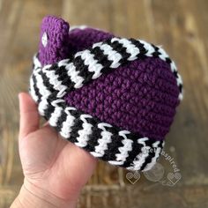 a hand holding a purple and black knitted hat