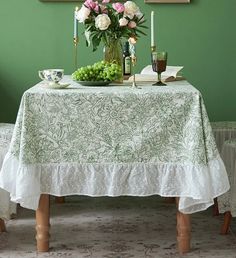 a table with flowers and candles on it in front of a green wall, next to two chairs