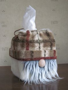 a stuffed animal wearing a plaid hat on top of a wooden table next to a tissue dispenser