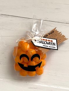 a bag filled with orange candies sitting on top of a white wooden table next to a tag that says happy halloween