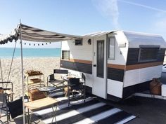 an rv parked on the beach next to some chairs