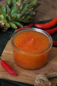 an orange sauce in a glass jar next to some red peppers and pineapples