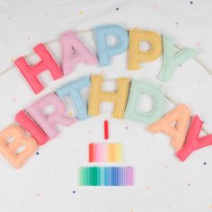 happy birthday spelled out with colorful letters on a white tablecloth and rainbow colored candles