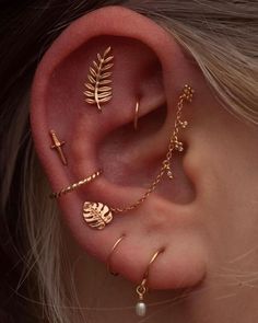 a close up of a person wearing ear piercings with leaves and beads on them