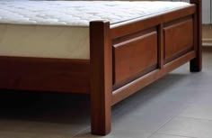 a wooden bed frame with no mattress on it in a room that has tile flooring