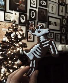 a hand holding a decorated cookie in front of a christmas tree with pictures on the wall