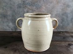 a white vase sitting on top of a wooden table next to a gray wall in the background