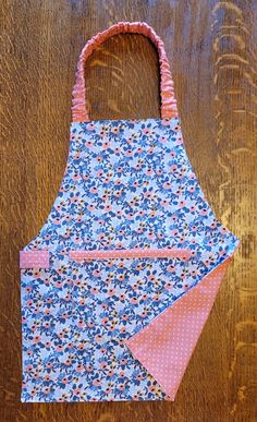 an apron made out of fabric on top of a wooden table with a pink and blue flowered pocket