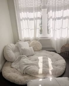 a large round bed in front of a window with white curtains and pillows on it