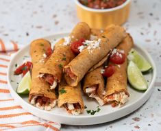 several burritos on a plate with salsa and lime wedges