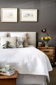 a bed with white sheets and pillows in a bedroom next to two framed pictures on the wall