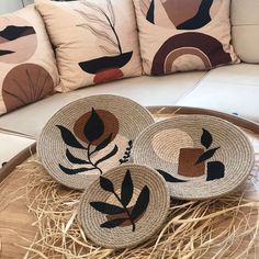 three woven placemats sitting on top of a wooden table next to pillows and straw