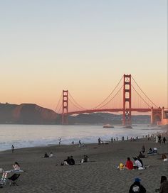 many people are sitting on the beach near the water and under the golden gate bridge