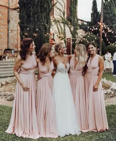 bridesmaids in pink dresses standing together and laughing at each other with string lights behind them