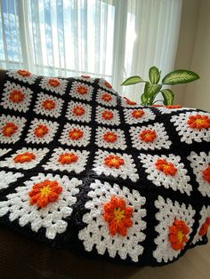 a black and white crocheted blanket with orange flowers on it next to a window