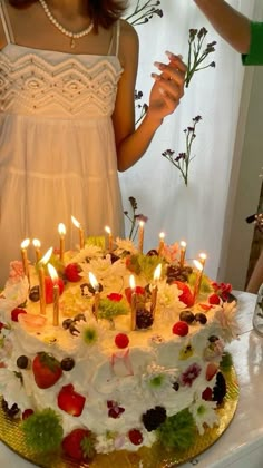 a woman standing in front of a cake with lit candles on it and flowers behind her