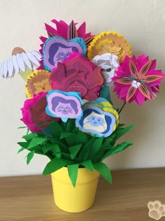 a yellow vase filled with paper flowers on top of a wooden table next to a white wall