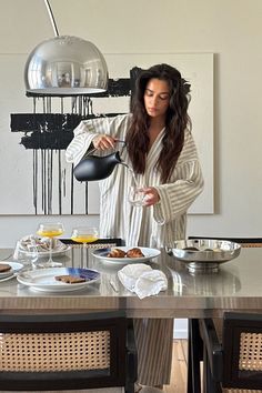 a woman pouring water into a bowl on top of a dining room table filled with food