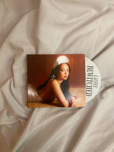 the cd is laying on top of the white sheeted bed spread, with an image of a woman wearing a headband